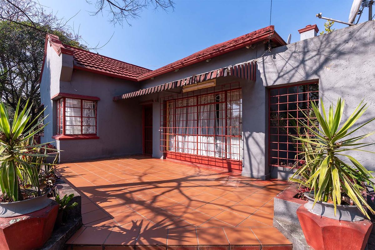 A rear exterior view of the house featuring a tiled patio area, security bars on windows, and a traditional tiled roof.
