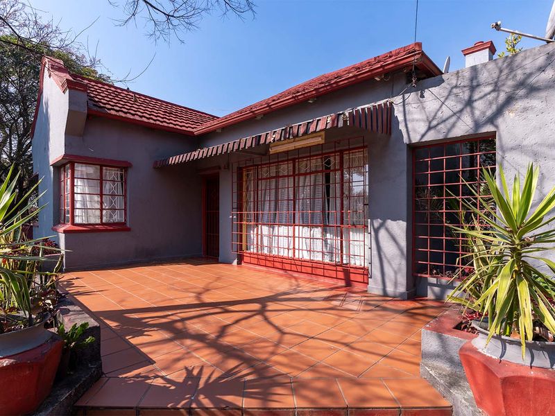 A rear exterior view of the house featuring a tiled patio area, security bars on windows, and a traditional tiled roof.
