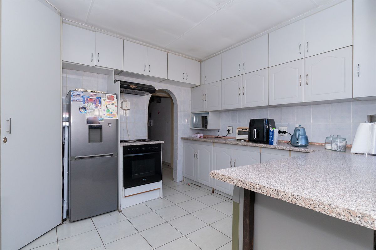 A functional kitchen featuring white cabinetry, laminate countertops, tiled flooring, and a classic archway entrance, offering a practical layout for daily meal preparation.