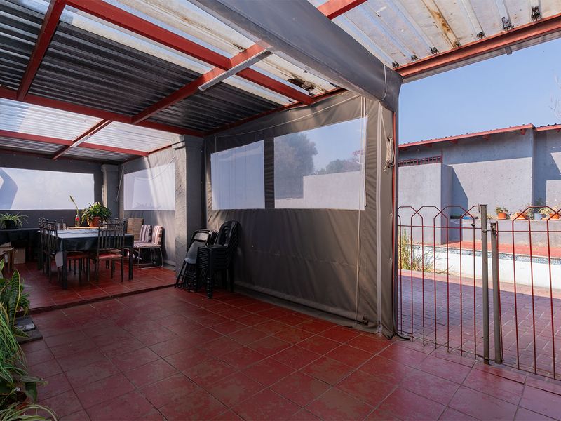 A covered outdoor patio area featuring tiled flooring, retractable weather blinds, and direct access to the swimming pool area.