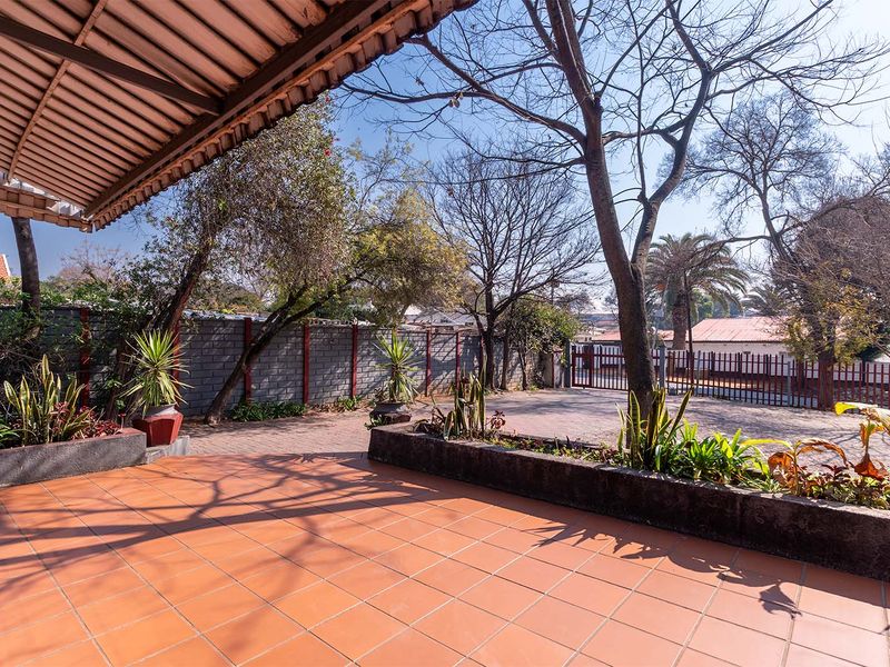 A spacious covered patio area featuring tiled flooring and built-in concrete planter boxes, overlooking a paved driveway and garden space.