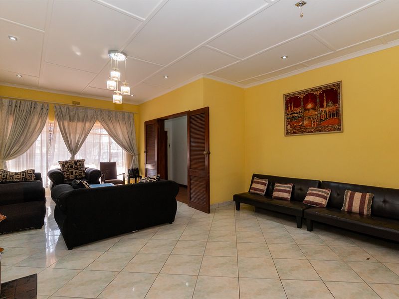 Spacious living room featuring tiled flooring, a coffered ceiling with recessed lighting, and louvered wooden doors leading to adjacent areas.