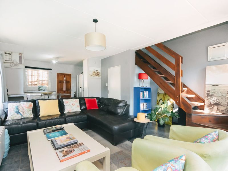 Open plan living area featuring a wooden staircase, tiled flooring, and a functional kitchen space in the background.