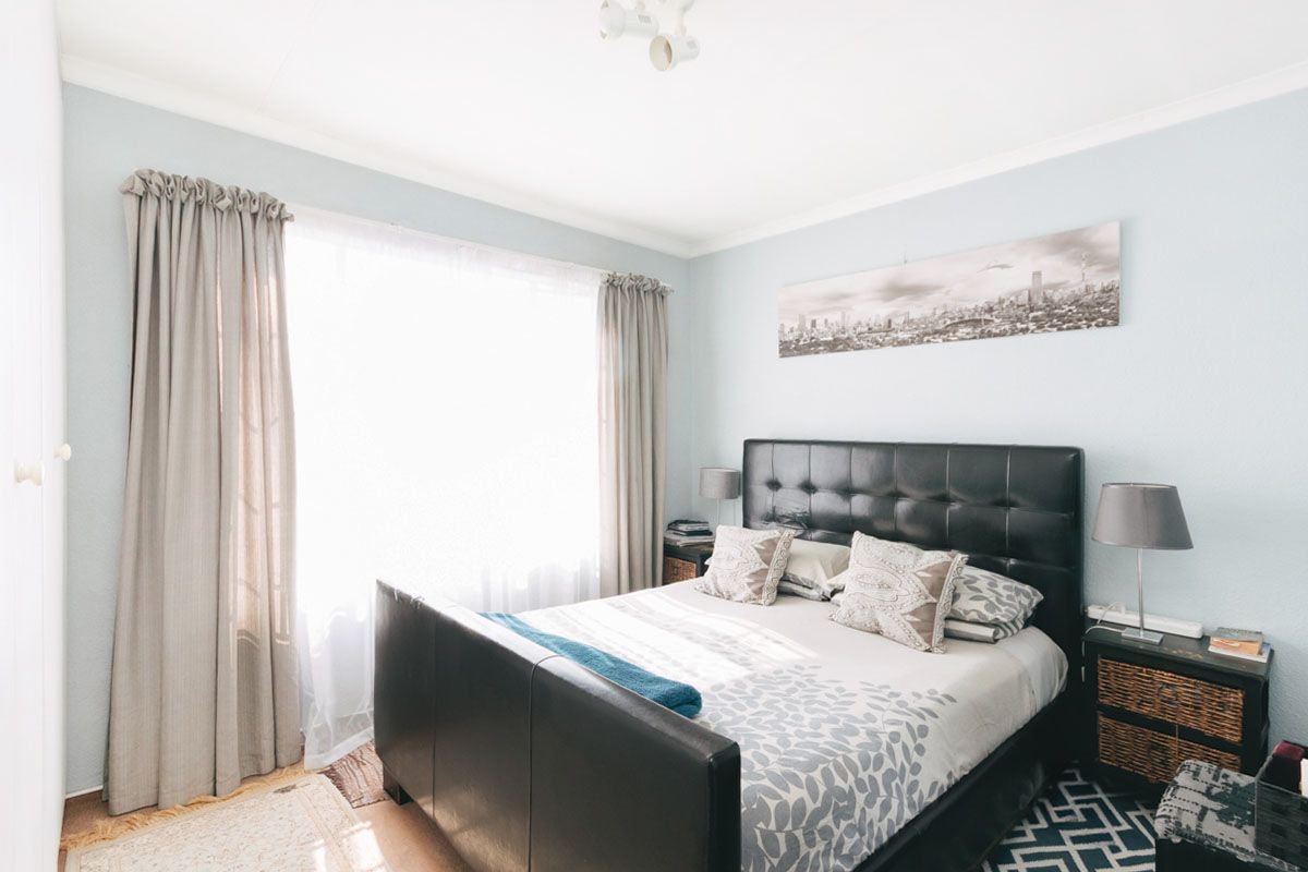 A well-lit bedroom featuring neutral wall tones, coving, and a large window with curtain tracks.