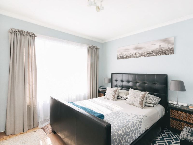 A well-lit bedroom featuring neutral wall tones, coving, and a large window with curtain tracks.