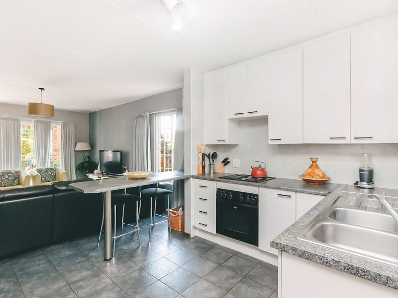 Open-plan kitchen and living area featuring white cabinetry, dark laminate countertops, integrated appliances, and tiled flooring, creating a functional and connected living space.