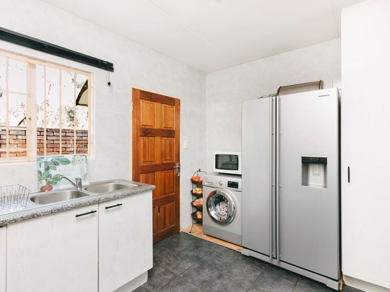 Functional laundry area featuring tiled walls, durable floor tiles, built-in cabinetry with a double sink, and direct access to the exterior.