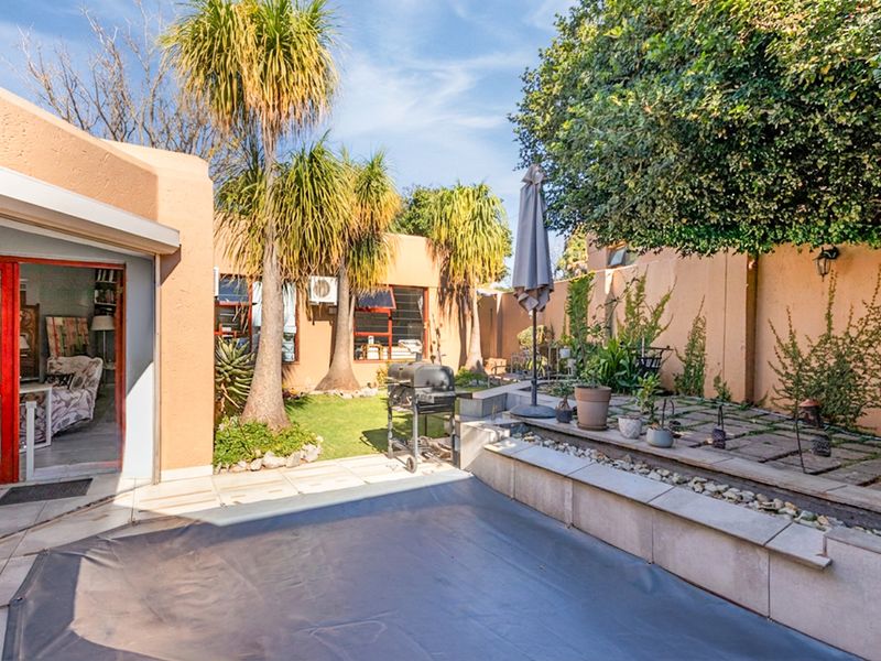 A private outdoor pool area featuring a covered swimming pool, paved patio space, raised stone planters, and established garden landscaping.