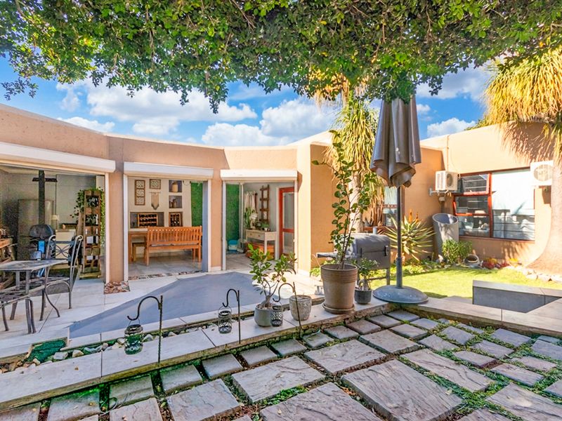 A well-maintained outdoor patio area featuring paved flooring, integrated garden landscaping, and direct access to the home through multiple sliding door entrances.