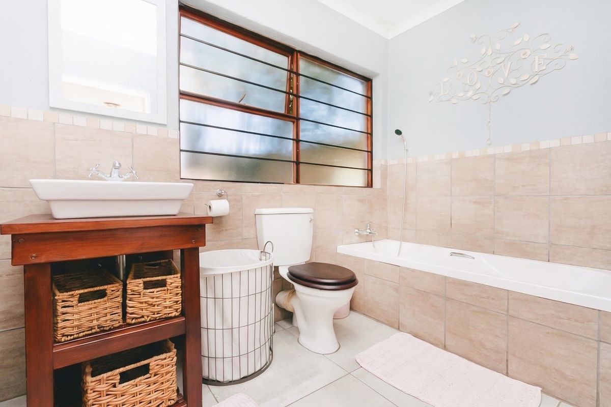 A well-maintained bathroom featuring a vessel sink on a wooden vanity, a standard bathtub with a handheld shower mixer, and neutral wall tiling.