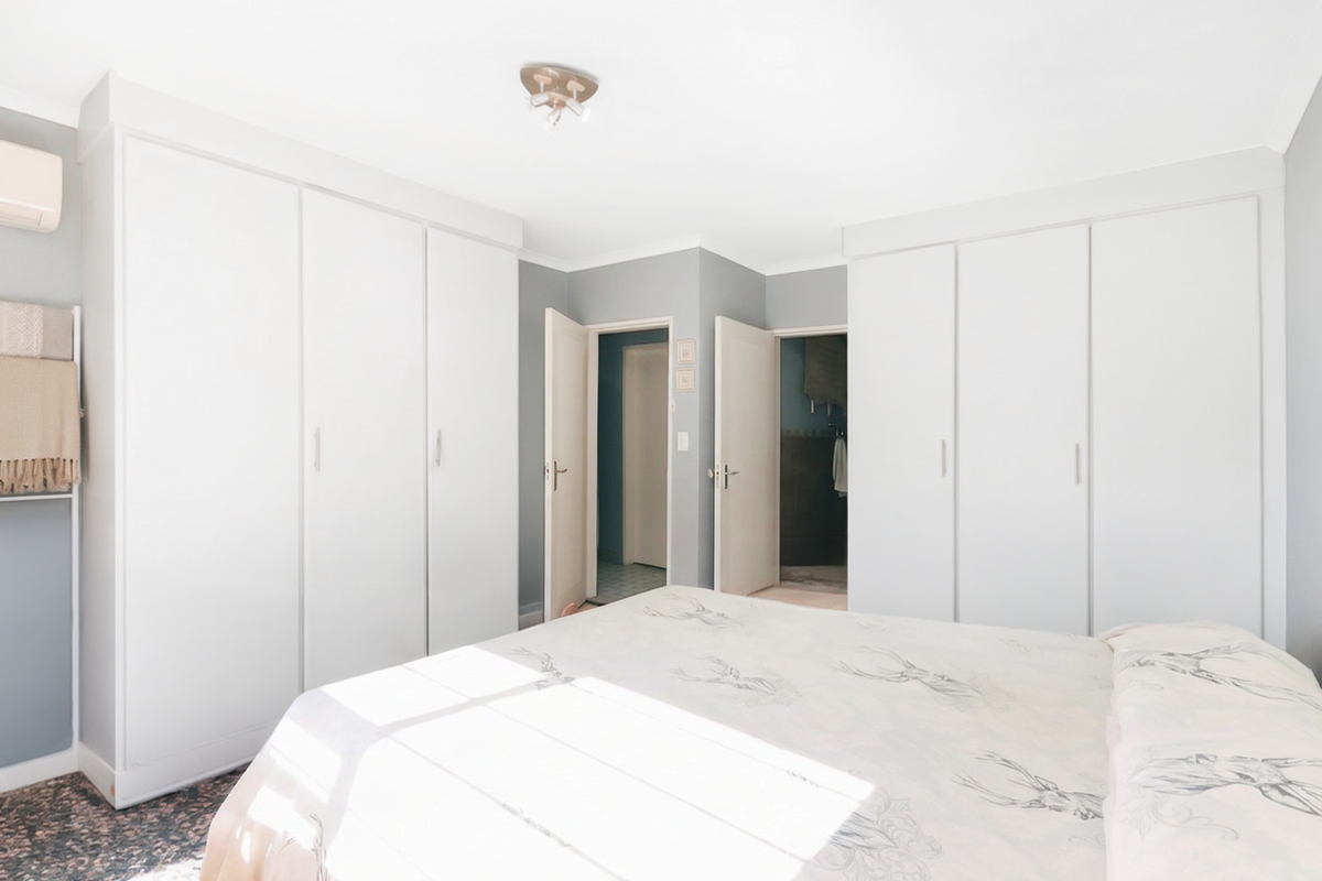 A well-maintained bedroom featuring extensive built-in cupboard storage, an integrated air conditioning unit, and neutral wall finishes.