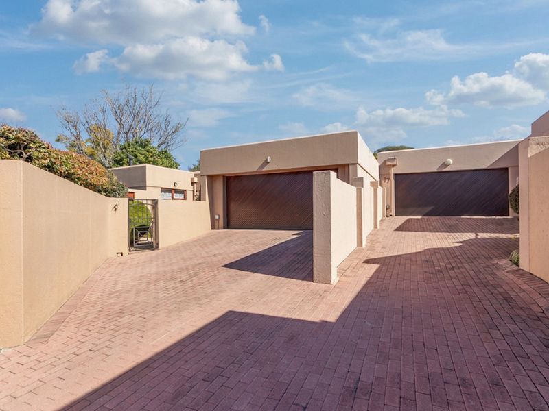 Front exterior view of the property featuring a paved driveway leading to double garage doors and secure boundary walls.