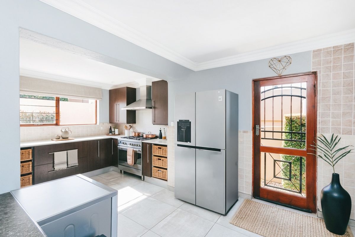 Modern kitchen featuring dark wood cabinetry, stainless steel gas stove, extractor fan, tiled splashback, and direct access to the exterior via a secure timber door.