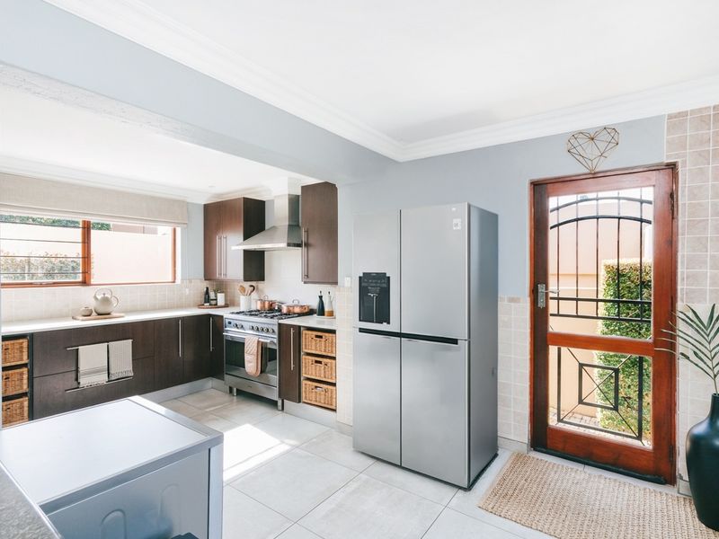 Modern kitchen featuring dark wood cabinetry, stainless steel gas stove, extractor fan, tiled splashback, and direct access to the exterior via a secure timber door.