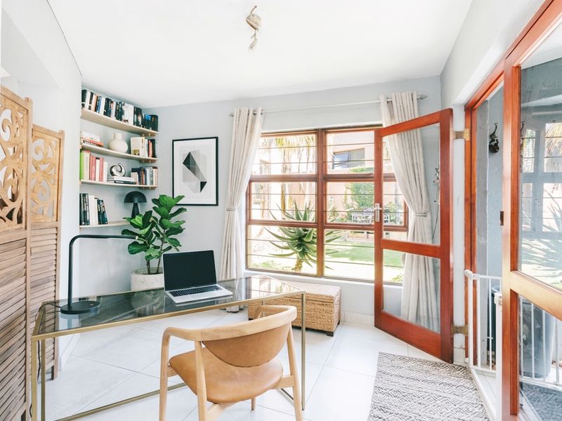 A bright home office featuring built-in shelving, tiled flooring, and direct access to the garden through a timber-framed door.