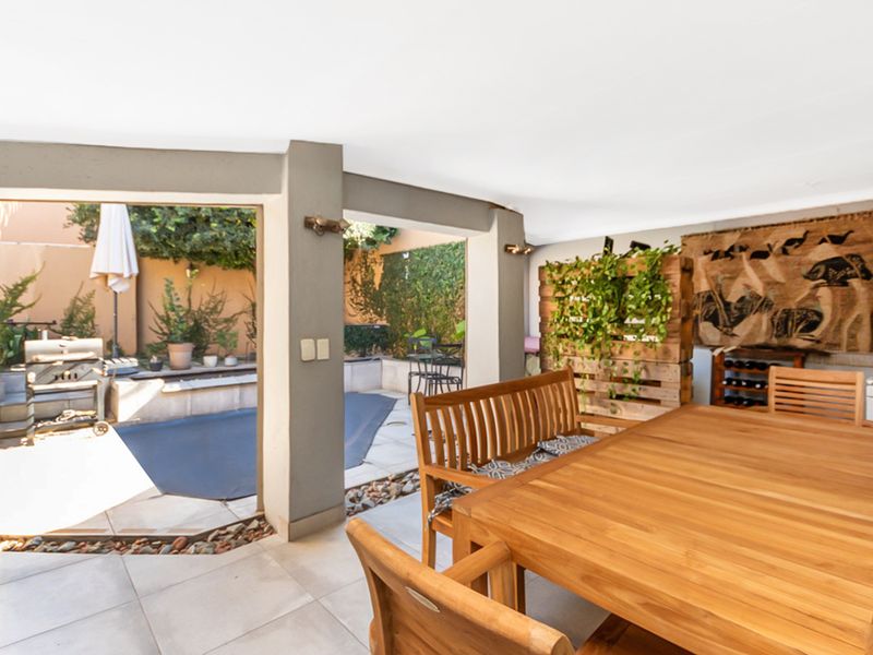 A covered outdoor patio area featuring tiled flooring and direct access to a rear garden space with a built-in stone garden bed.
