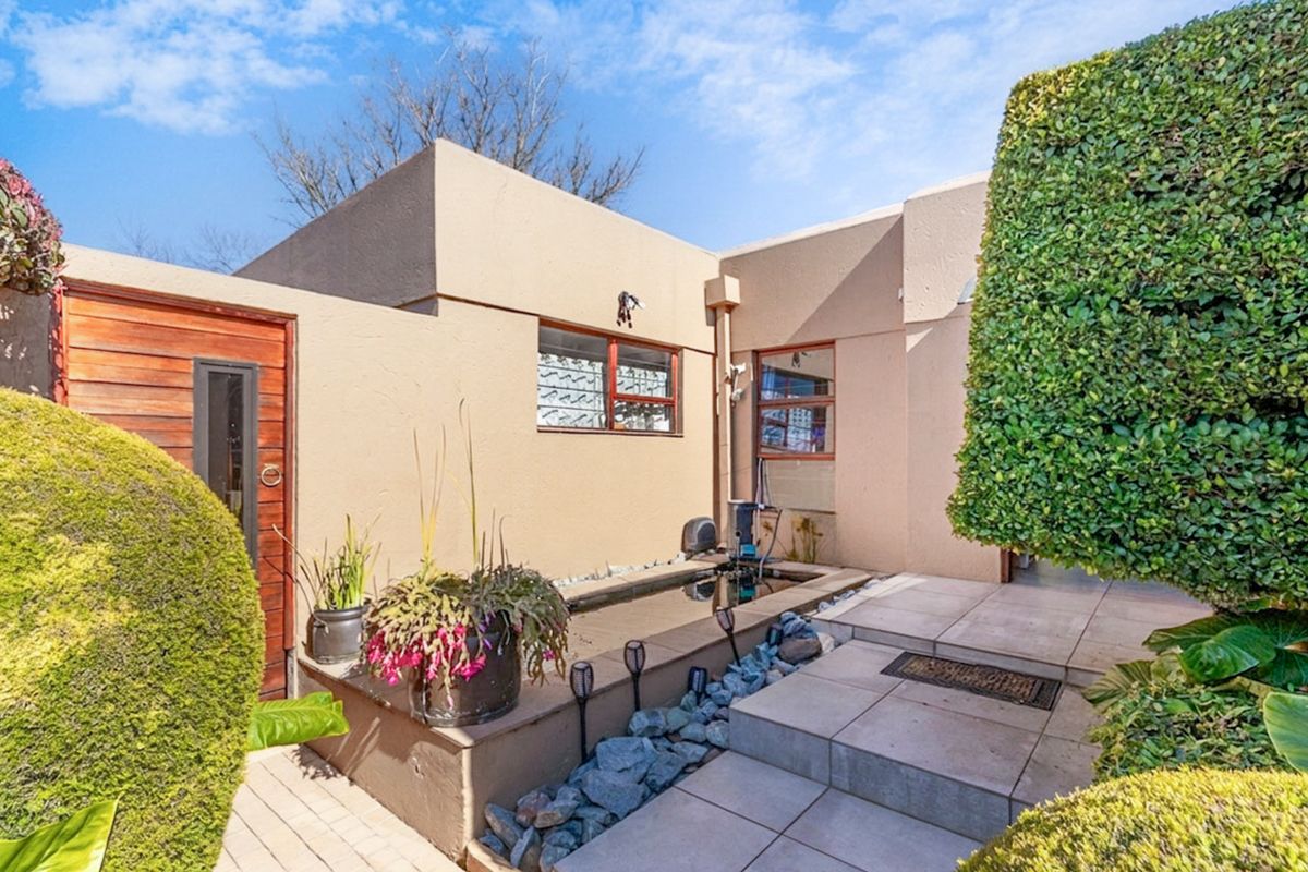 A private rear courtyard featuring a built-in water feature, tiled patio area, and well-maintained landscaping with mature hedges.