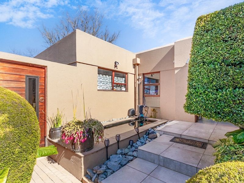 A private rear courtyard featuring a built-in water feature, tiled patio area, and well-maintained landscaping with mature hedges.