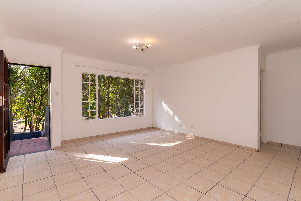 A bright, empty living room featuring neutral tiled flooring, large windows with natural light, and direct access to an outdoor area.