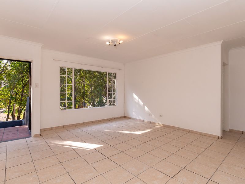 A bright, empty living room featuring neutral tiled flooring, large windows with natural light, and direct access to an outdoor area.