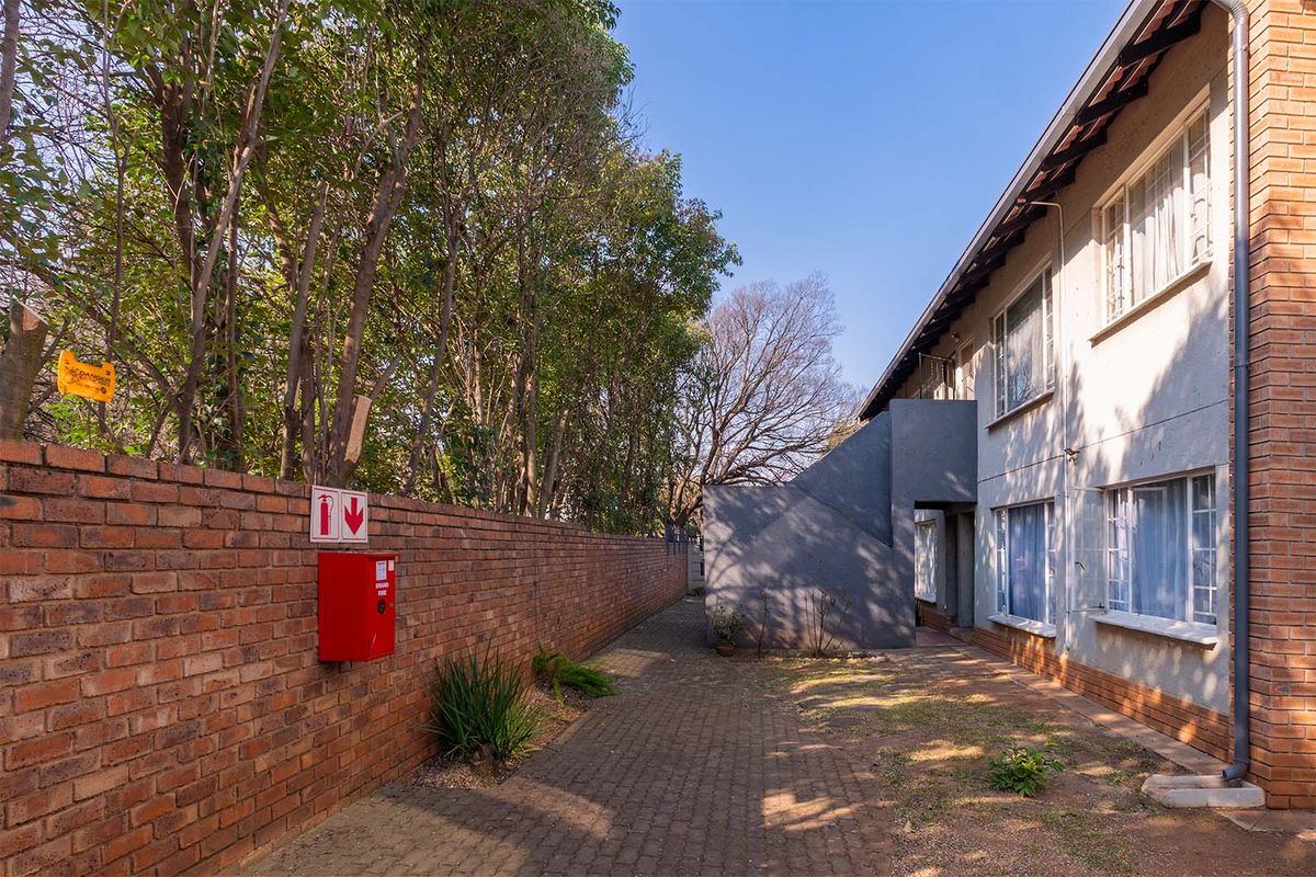 Rear exterior view of the apartment building featuring a paved walkway, brick boundary wall, and external staircase access.