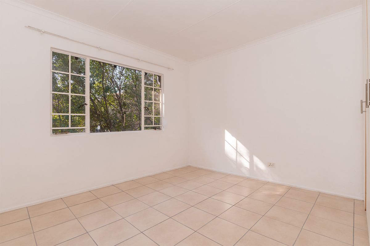 A bright, empty bedroom featuring neutral tiled flooring, a built-in wardrobe, and large casement windows allowing for natural light.