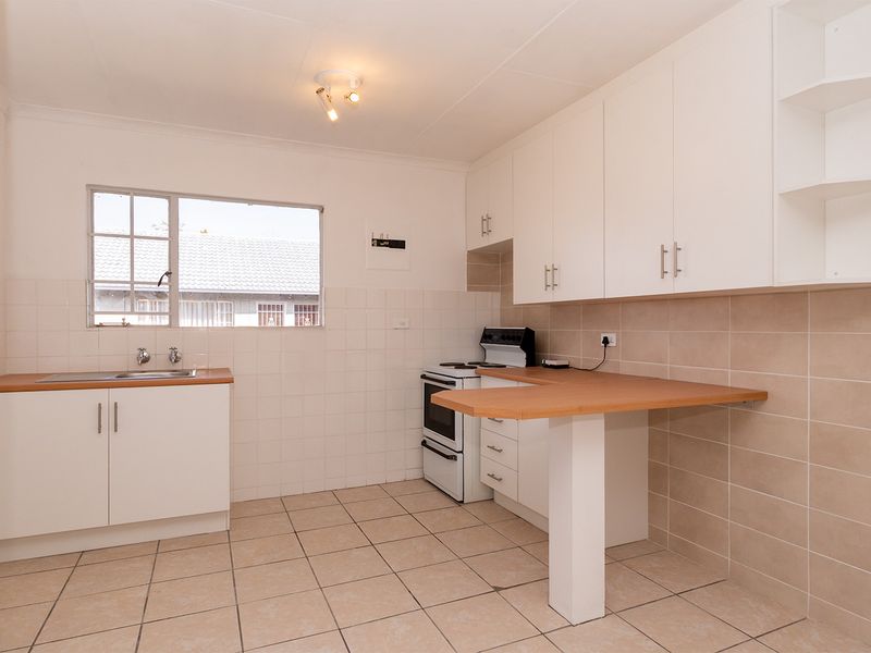 A clean, functional kitchen featuring white cabinetry, a breakfast bar, tiled backsplash, and tiled flooring, providing a practical space for cooking and dining.