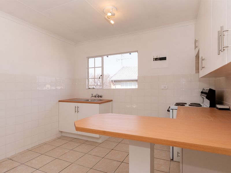 A functional, empty kitchen featuring white cabinetry, laminate countertops, tiled splashbacks, and tiled flooring, offering a clean canvas for potential updates.