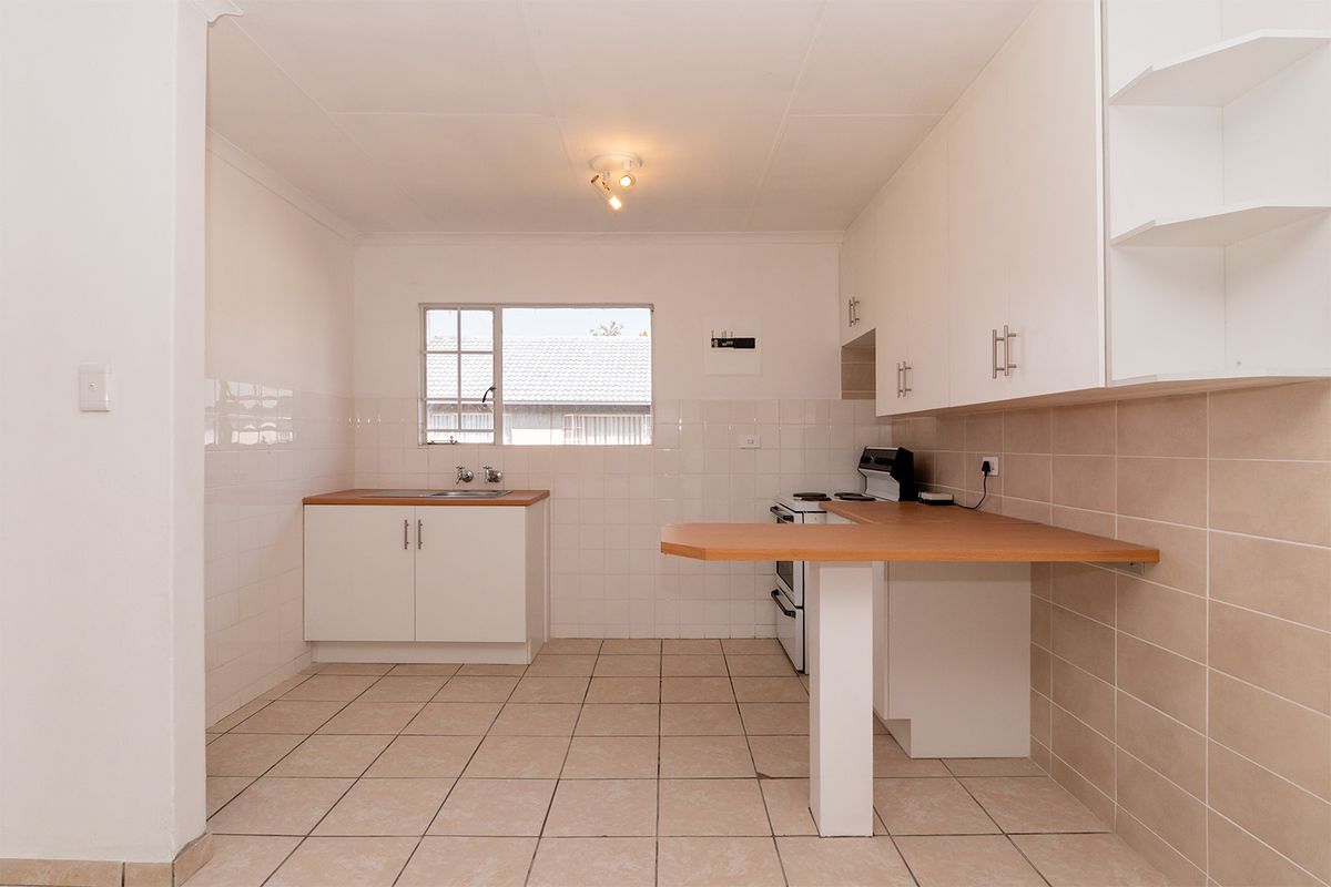 A clean, functional kitchen featuring white cabinetry, laminate countertops, a breakfast bar, and tiled flooring, offering a bright and practical workspace.
