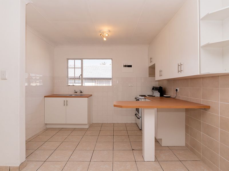 A clean, functional kitchen featuring white cabinetry, laminate countertops, a breakfast bar, and tiled flooring, offering a bright and practical workspace.