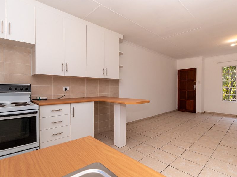 An open-plan kitchen and living area featuring tiled flooring, white cabinetry, a breakfast bar, and a freestanding stove in a clean, vacant space.