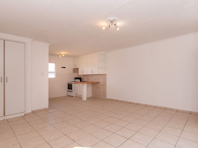 An open-plan living and kitchen area featuring neutral tiled flooring, built-in cabinetry, and a functional kitchen layout in a clean, vacant space.