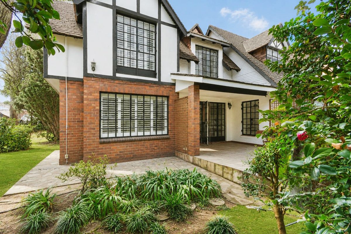 Rear view of a charming townhouse featuring a brick and timber-framed facade, stone-paved patio area, and established garden surroundings.