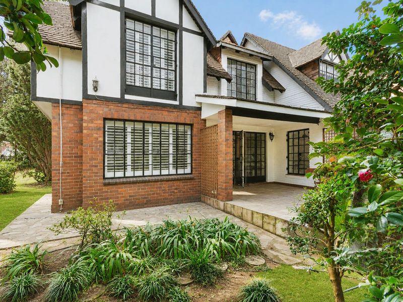 Rear view of a charming townhouse featuring a brick and timber-framed facade, stone-paved patio area, and established garden surroundings.