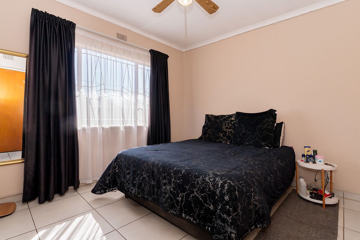 A functional bedroom featuring tiled flooring, a ceiling fan, and a window with security bars, providing a neutral base for personalization.
