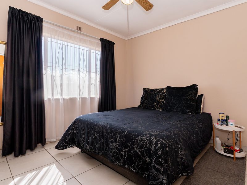 A functional bedroom featuring tiled flooring, a ceiling fan, and a window with security bars, providing a neutral base for personalization.