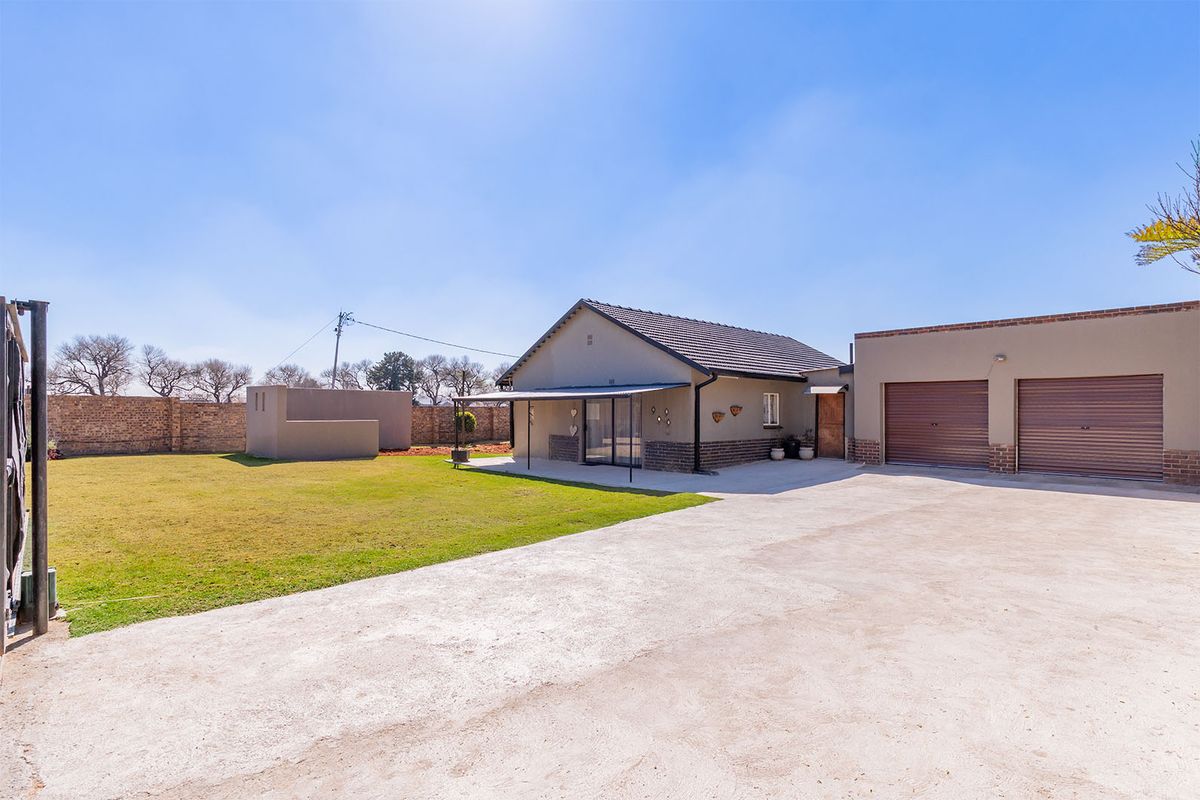 Rear view of the property featuring a spacious lawn, concrete driveway, double garage, and a covered patio area.