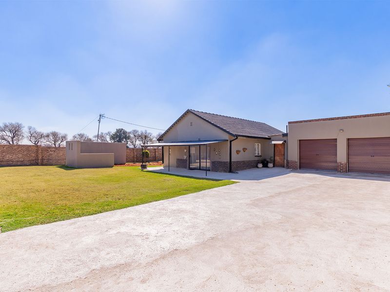 Rear view of the property featuring a spacious lawn, concrete driveway, double garage, and a covered patio area.