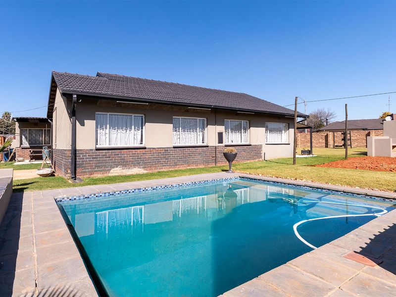 Rear view of the house featuring a swimming pool with paved surround, brick and plastered exterior walls, and a tiled roof.