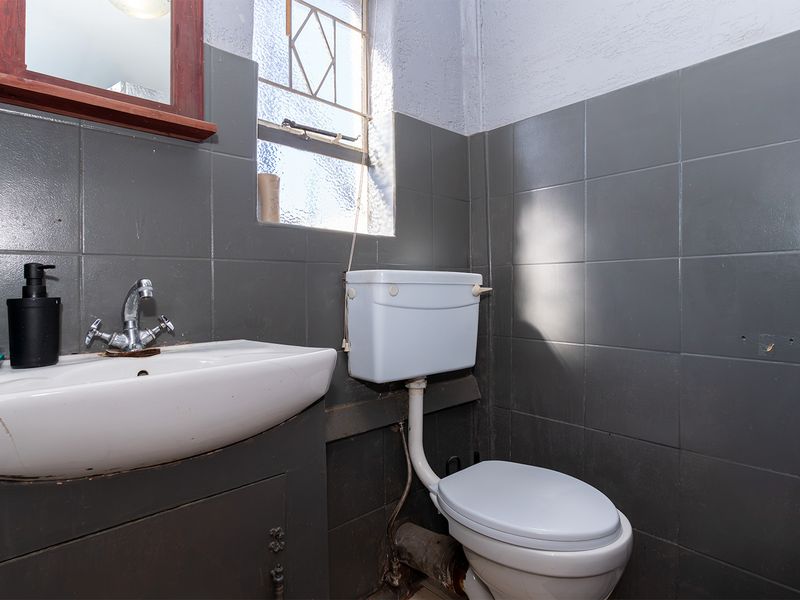 A compact bathroom featuring dark grey wall tiles, a white pedestal washbasin, and a standard toilet with exposed plumbing.