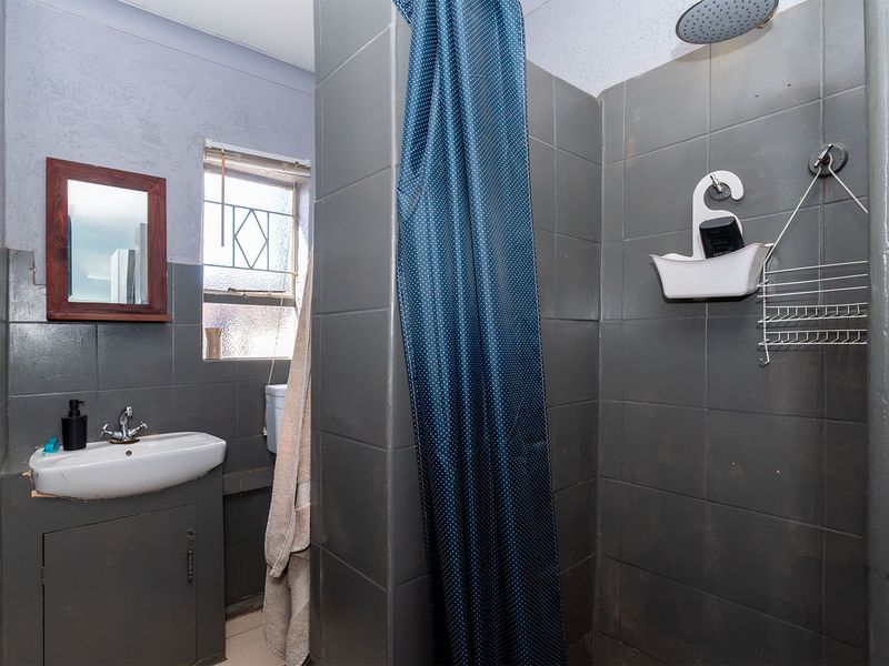 A functional bathroom featuring a wall-mounted basin with vanity cabinet and a tiled shower enclosure with a fixed shower head.
