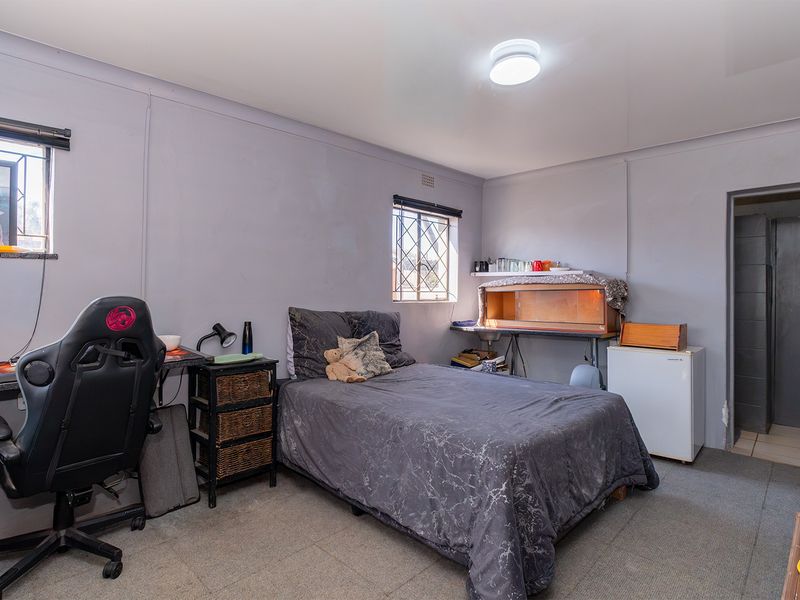 A functional bedroom featuring carpeted flooring, security bars on windows, and a central flush mount ceiling light.