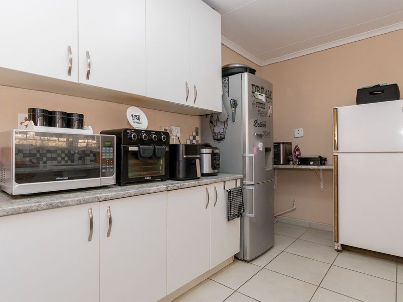A functional kitchen featuring white cabinetry, laminate countertops, and tiled flooring, providing ample storage and workspace for daily meal preparation.