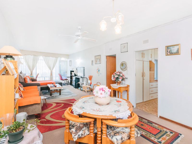 Spacious open-plan living and dining area featuring neutral carpeting, a ceiling fan, and direct access to a balcony through sliding glass doors.