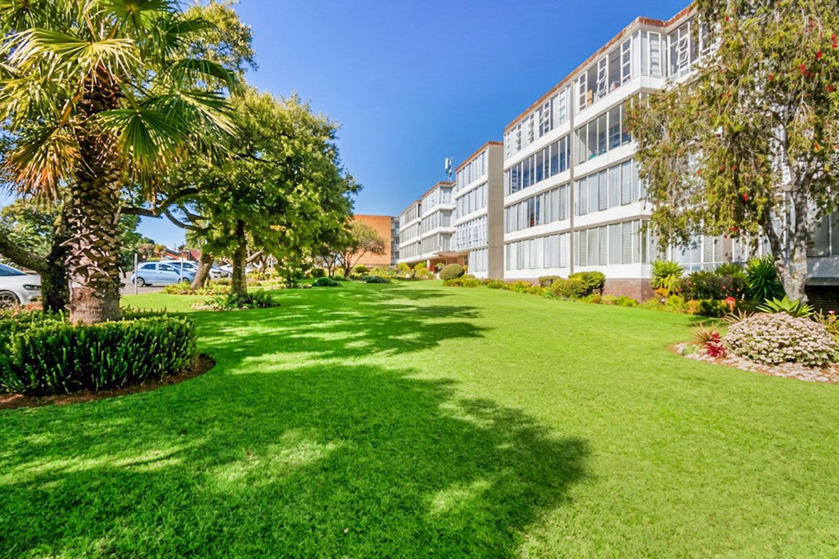 A well-maintained apartment building exterior featuring expansive green lawns, mature landscaping, and multiple levels of enclosed balconies.