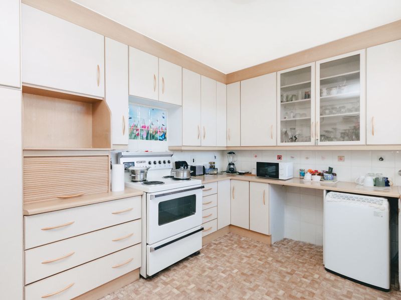 A functional kitchen featuring light-toned built-in cabinetry, a freestanding stove, tiled backsplash, and ample storage space with glass-fronted display cabinets.