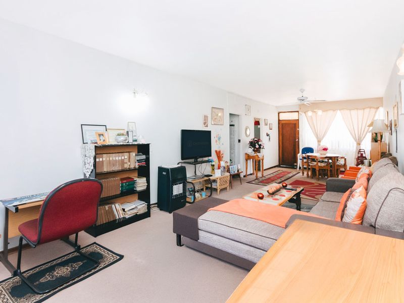 Spacious open-plan living and dining area featuring neutral carpeting, ceiling fan, and wall-mounted lighting, offering a versatile layout for comfortable daily living.