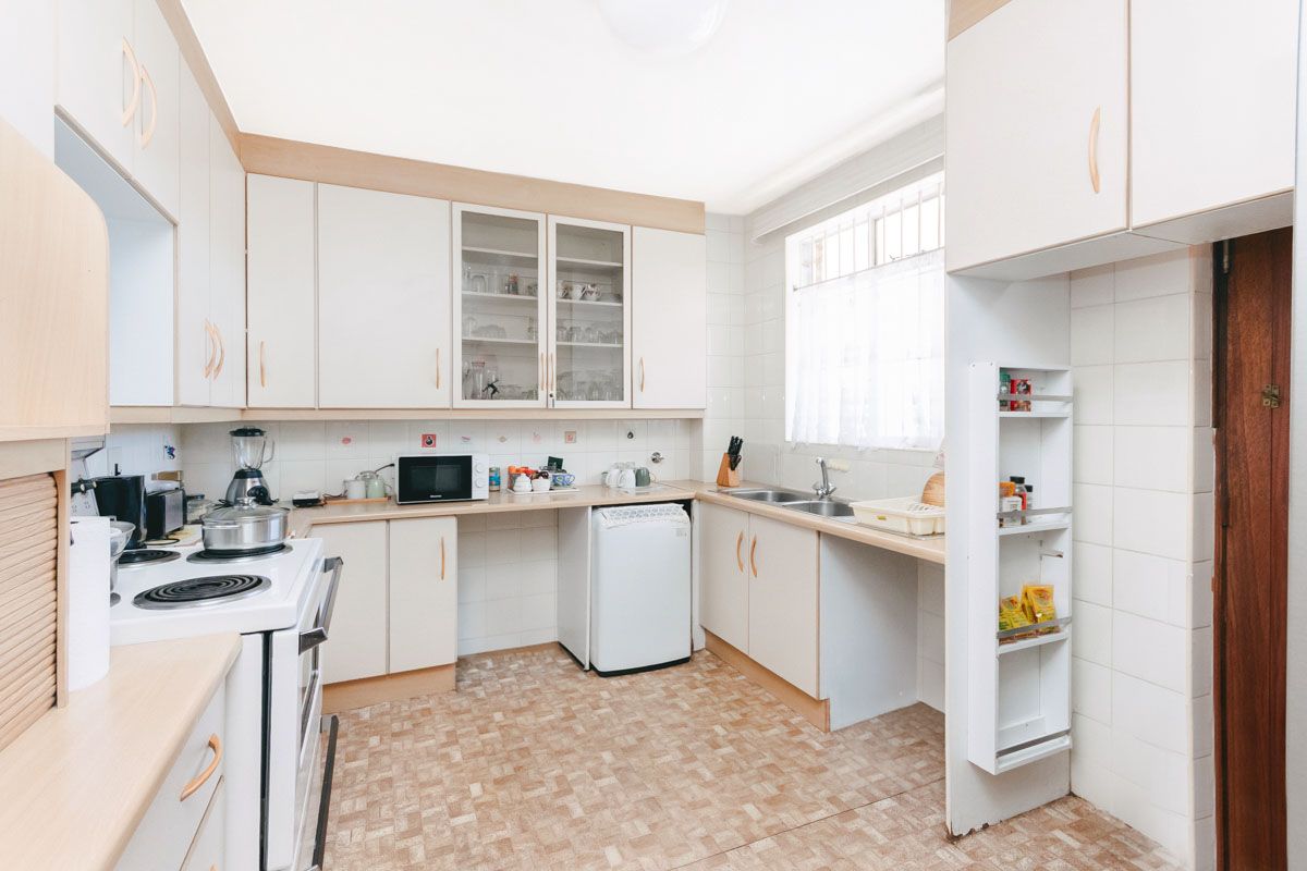 A functional kitchen featuring built-in cabinetry, a double sink, electric stove, and tiled finishes, offering a practical layout with potential for modern updates.