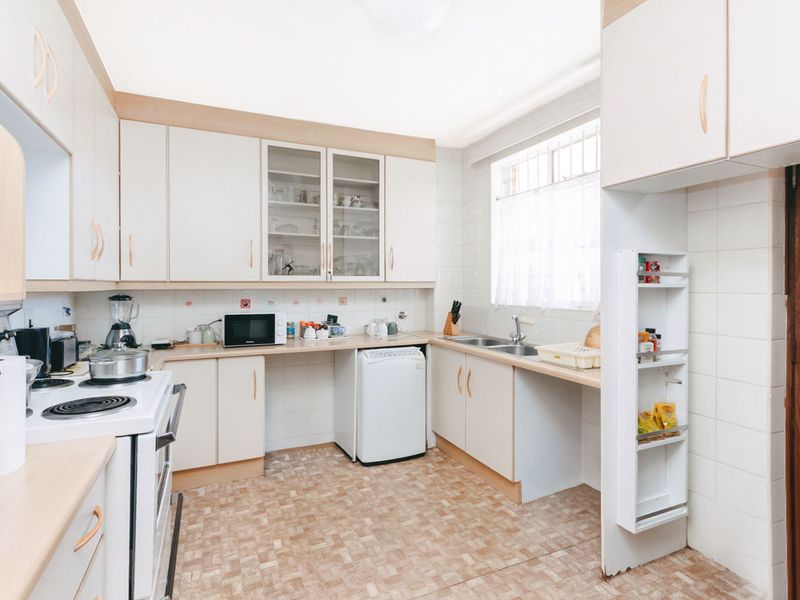 A functional kitchen featuring built-in cabinetry, a double sink, electric stove, and tiled finishes, offering a practical layout with potential for modern updates.