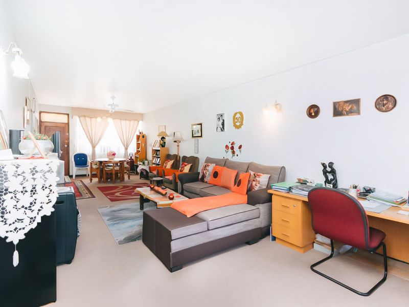 An open-plan living and dining area featuring neutral carpeting, wall-mounted lighting, and a ceiling fan, offering a versatile space for relaxation and dining.
